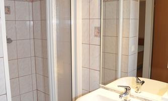 A clean bathroom with a sink, a shower cubicle, and bright tiles. There is also a large mirror and illuminated mirror lights.