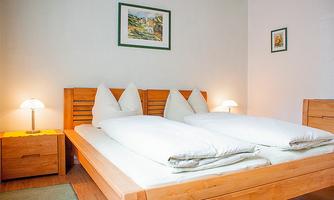 A bright bedroom with a double bed and two bedside tables. Decorative pictures hang on the walls, and there is soft lighting.