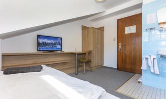 A cozy room with a television, a wooden wardrobe, and a chair. The bathroom is tiled in light blue and has a shower.