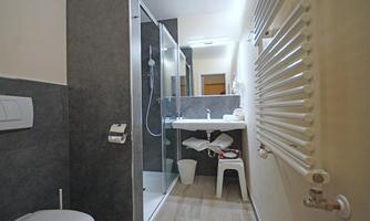 A modern bathroom with a shower and a sink. On the left side, there is a toilet and towels are visible.