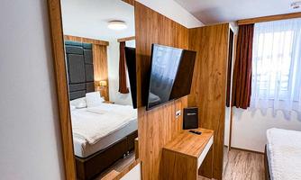 A modern room with wood paneling and a large mirror. There is a bed, a television, and a small table.