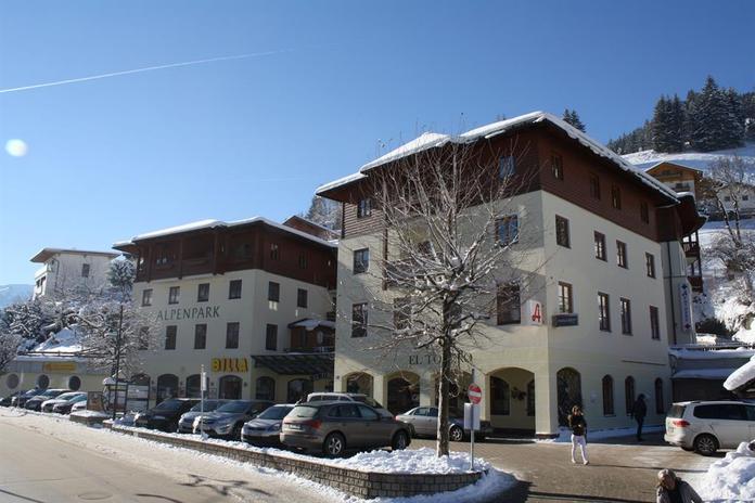 A picturesque building in winter, surrounded by snow-covered trees. The sun shines clearly over the scene, and the road is lightly trafficked.