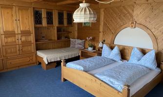 A cozy bedroom with wooden paneling and a double bed. There is also a single bed and a warm atmosphere.
