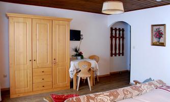 A cozy room with a wooden wardrobe, a dining table, and chairs. The walls are painted light and there is a beautiful ceiling lamp.