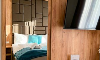 A modern hotel room with a large mirror and a flat-screen TV. The room features warm wooden colors and has an inviting bed with blue pillows.