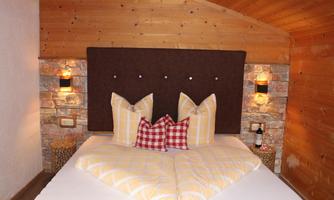 A cozy bedroom with a double bed and decorative cushions. The walls are made of wood and stone, creating a warm atmosphere.
