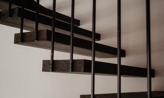A modern staircase with dark wooden steps and black railing bars. The background is designed to be simple and minimalist.