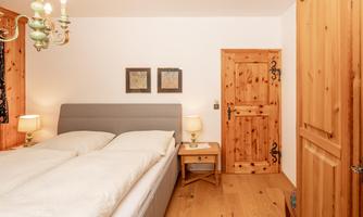 A cozy bedroom with a large bed and two nightstands. The walls are light, and there is a wooden panel with a beautiful door.