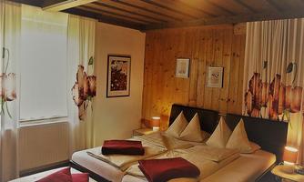 A cozy bedroom with wooden paneling and large windows. The bed is decorated with red cushions, creating an inviting atmosphere.