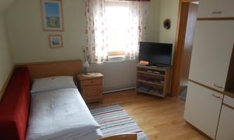 A cozy room with a single bed and a red sofa. There is a television, a table, and large windows with curtains.