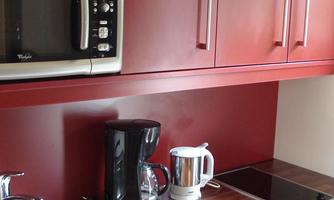 A modern kitchen with a red lacquered design. It includes a microwave, a kettle, a coffee machine, and a sink.