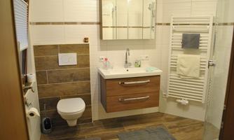 A modern bathroom with a white wall and wood-look tiles. It features a sink, a mirror, and a towel radiator.