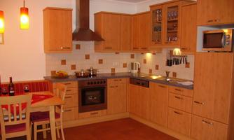 A modern kitchen with wooden furniture and elegant appliances. The dining area has a table with colorful chairs and a warm atmosphere.