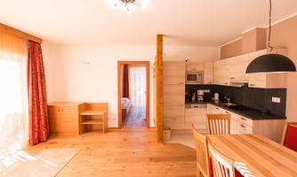 A modernly furnished kitchen with a dining area and wooden floor. Light pours into the room through large windows.