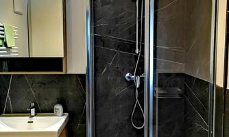 A modern bathroom with a glass shower cubicle and elegant dark wall cladding. Next to the shower stands a stylish wooden washstand.