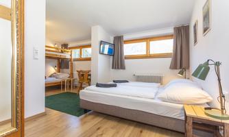 A cozy room with a double bed and a bunk bed. Large windows provide plenty of daylight.