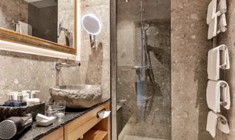 A modern bathroom with an elegant shower and a stylish sink. The walls are made of gray stone, and towels are neatly hung.