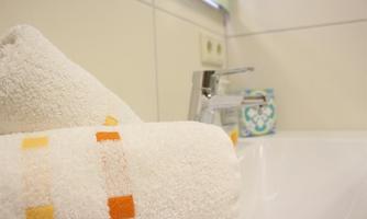 A freshly folded towel with colorful patterns lies next to a modern faucet. In the background, bright tiles and a soap dish are visible.