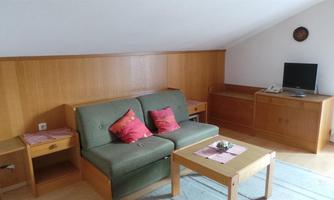 A cozy living room with a green sofa and red cushions. There is a wooden table, a TV, and a cabinet.