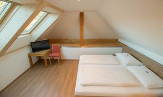A modern room with two single beds and a cozy seating area.  
Large windows let in plenty of daylight and create a friendly atmosphere.
