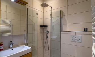 A modern bathroom with a glass shower and a sink. The walls are brightly tiled, and the room appears clean and tidy.