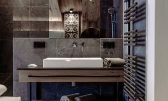 A modern bathroom with elegant tiles and a stylish wooden ceiling. The sinks are located on a simple table, while towels are neatly stacked.