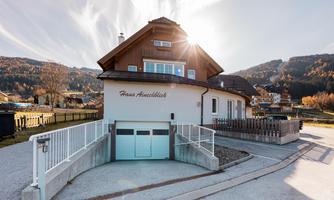 A modern house with a spacious garage and a well-maintained entrance. In the background, gentle hills and a beautiful landscape can be seen.