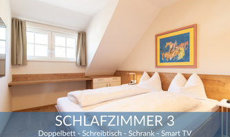 A cozy bedroom with a double bed, a desk, and a wardrobe. There is a window with curtains and a smart TV on the wall.