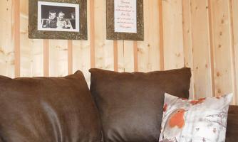 A cozy sofa with brown fabric and a decorative cushion. Picture frames with photos and a saying hang on the wall.