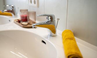 A modern bathroom with a shiny faucet and a white sink. A yellow towel and some decorative items give the room an inviting atmosphere.
