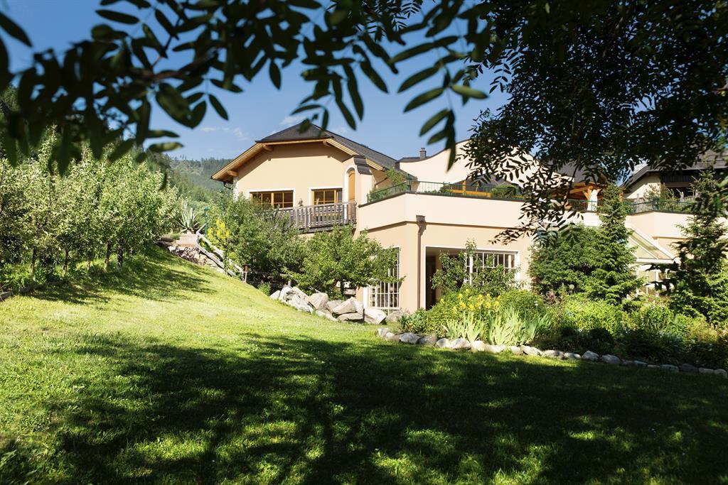 A charming house surrounded by lush greenery and trees. The sun is shining, creating a pleasant atmosphere in the garden.