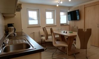 A modern kitchen with a dining area. The room is bright and friendly, equipped with a table and several chairs.