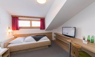 A cozy room with a double bed and a desk. It has large windows with red curtains and is decorated in a modern style.