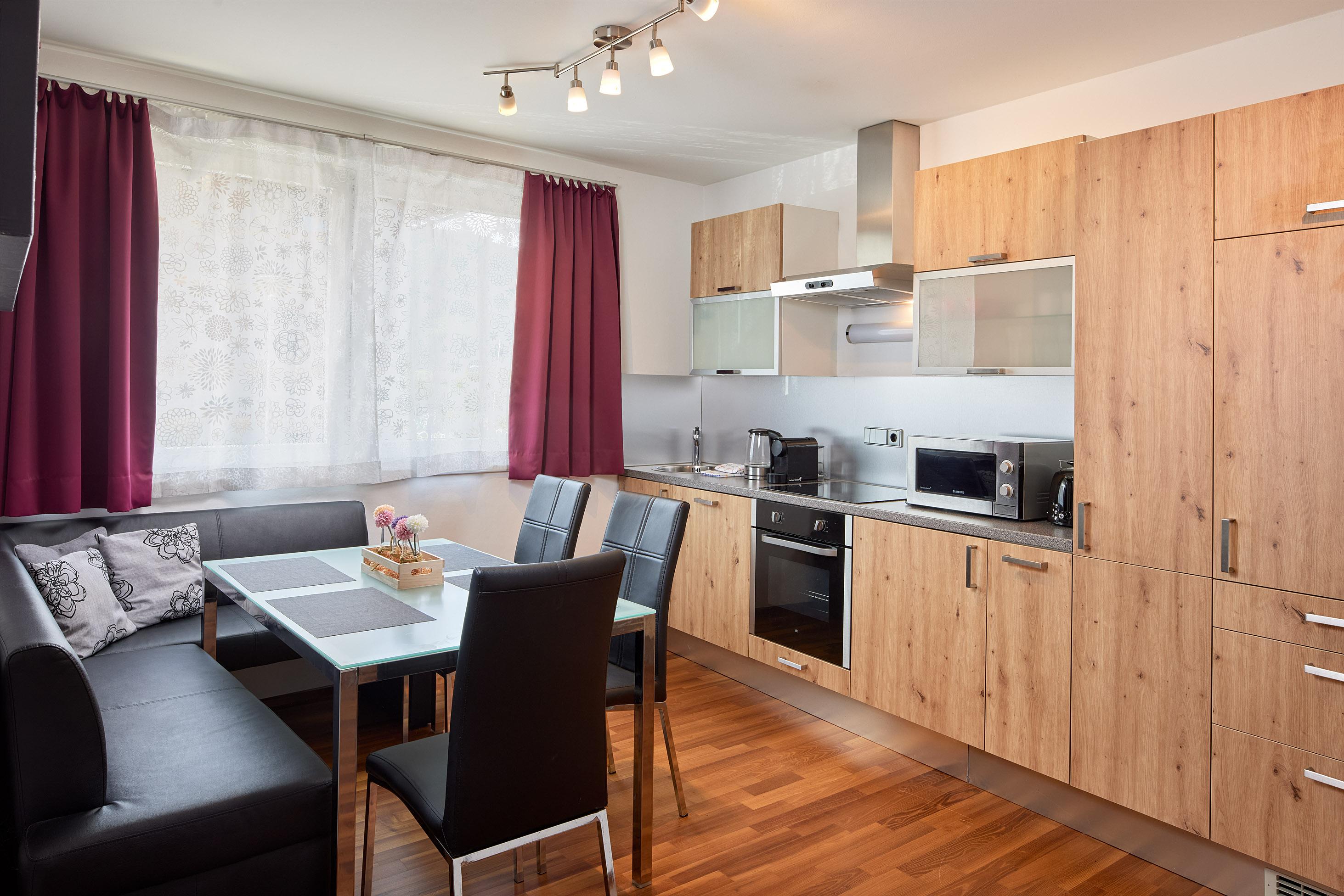 A modern kitchen with wooden cabinets and stainless steel appliances. A dining area with a table and four chairs next to it.