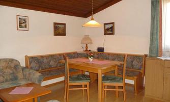 A cozy living space with a seating area and a dining table. The walls are decorated with pictures and large windows let in plenty of light.
