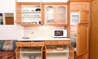 A modern kitchen with wooden cabinets and a built-in refrigerator. The upper part displays dishes and glasses, while the lower part stores plates and bowls.