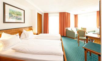 A bright room with two single beds and a cozy seating area. Large windows provide plenty of daylight and an inviting space.