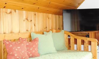 A cozy seating area with wooden paneling. Colorful cushions are laid on the bench, and a TV is mounted on the wall.