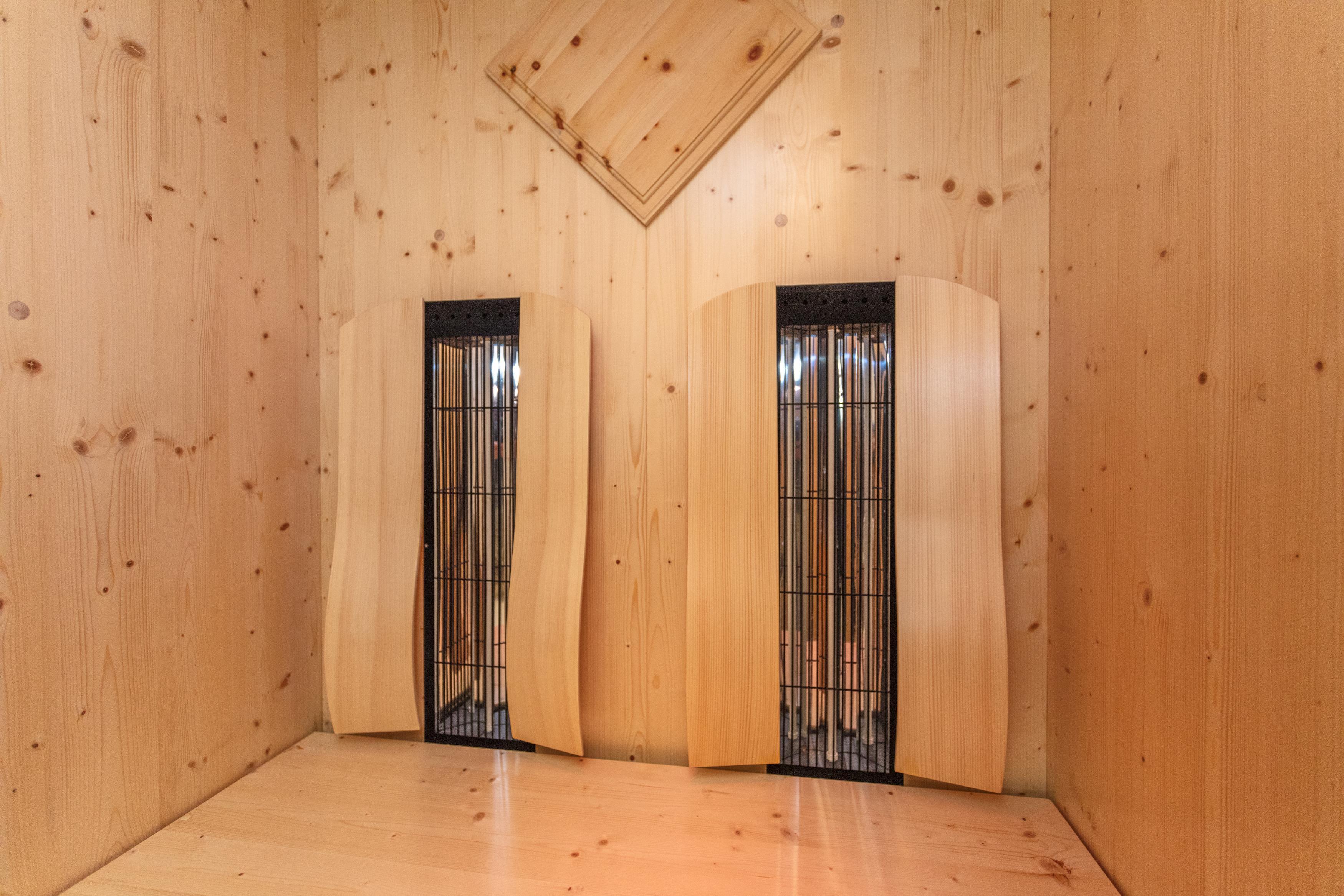 A minimalist room with wooden walls. Two curved wooden panels stand against the walls.