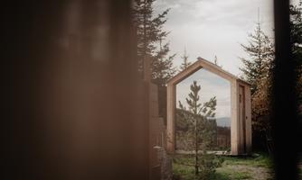 A modern wooden house stands among trees. There is an unobstructed view of the surroundings through the open structure.