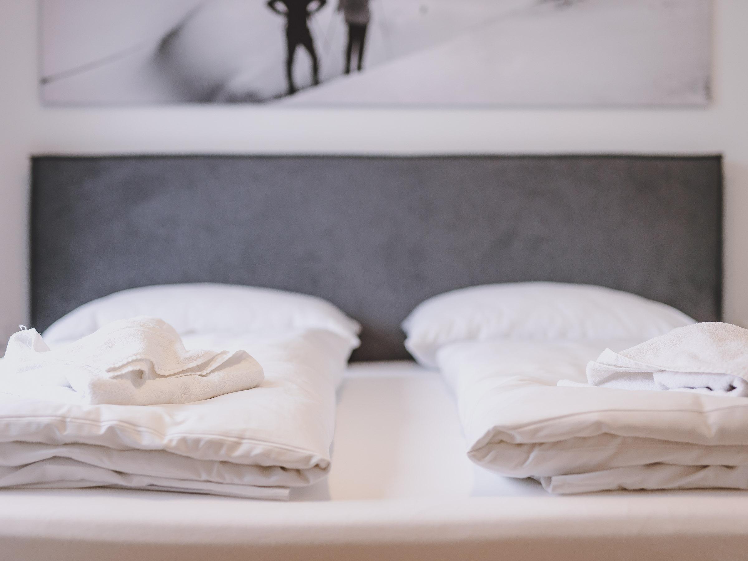 A cozy bedroom with two beds and white bedspreads. In the background, a minimalist picture can be seen.