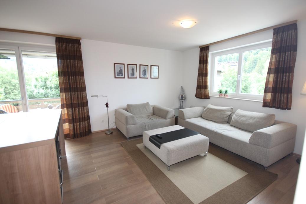 A bright living room with two sofas and a coffee table. Windows overlooking the outdoor area and decorative pictures on the wall.