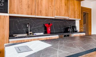 Modern kitchen with wooden cabinets and an elegant black countertop. A red decorative object adds a splash of color.