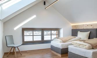 A modern bedroom with two single beds and a chair. Large windows provide plenty of daylight and a friendly atmosphere.