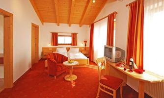 A cozy room with wooden walls and a red carpet. There is a large bed, a television, and a small table with chairs.