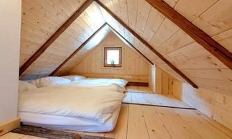 A cozy attic bedroom with wooden walls and floors. There are two beds and a small window that lets light in.