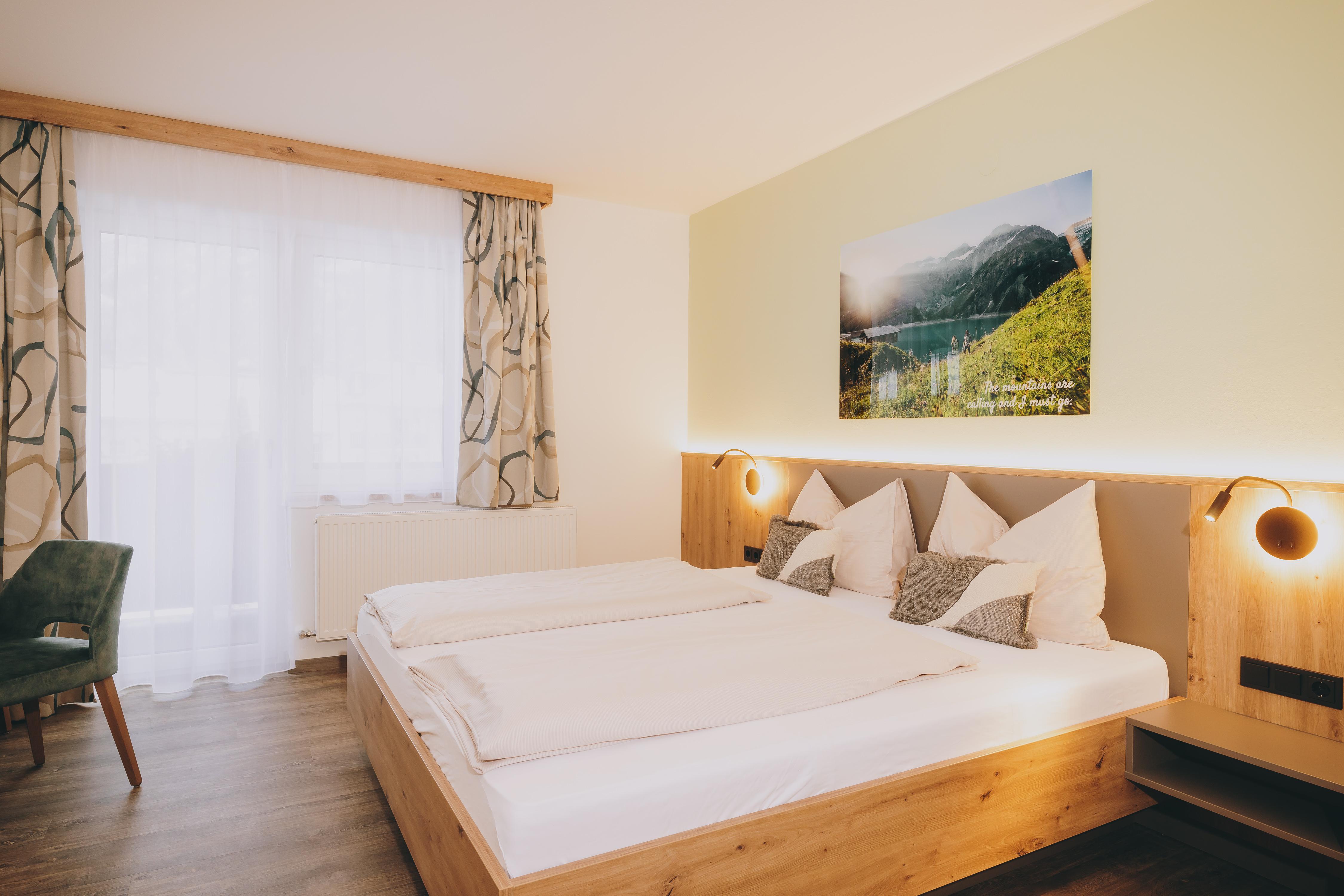 A modern bedroom with two single beds and wooden details. Large windows provide plenty of light, and a landscape painting hangs on the wall.