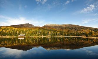 A tranquil lake, surrounded by colorful autumn trees and mountains. The reflective surface of the water showcases a beautiful natural scenery.