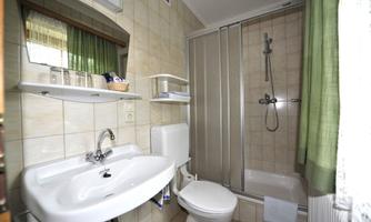 A modern bathroom with a shower, a sink, and a toilet. The walls are light-tiled, and green curtains add a fresh accent.