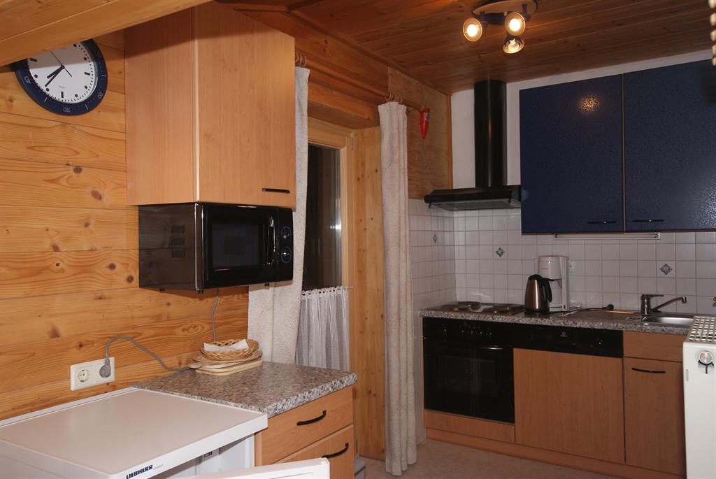 A cozy kitchen with wooden paneling, equipped with modern appliances. The furnishings include a refrigerator, a microwave, and a stove.